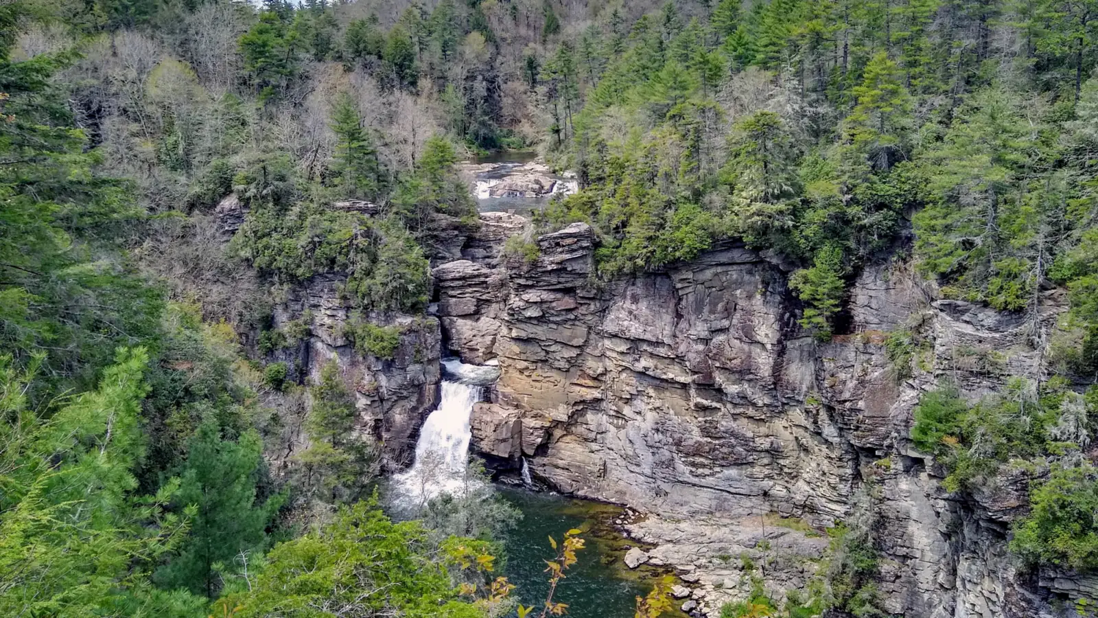 Linville Falls dropping into a pool below gray rock cliffs, with the upper falls visible behind and forest all around